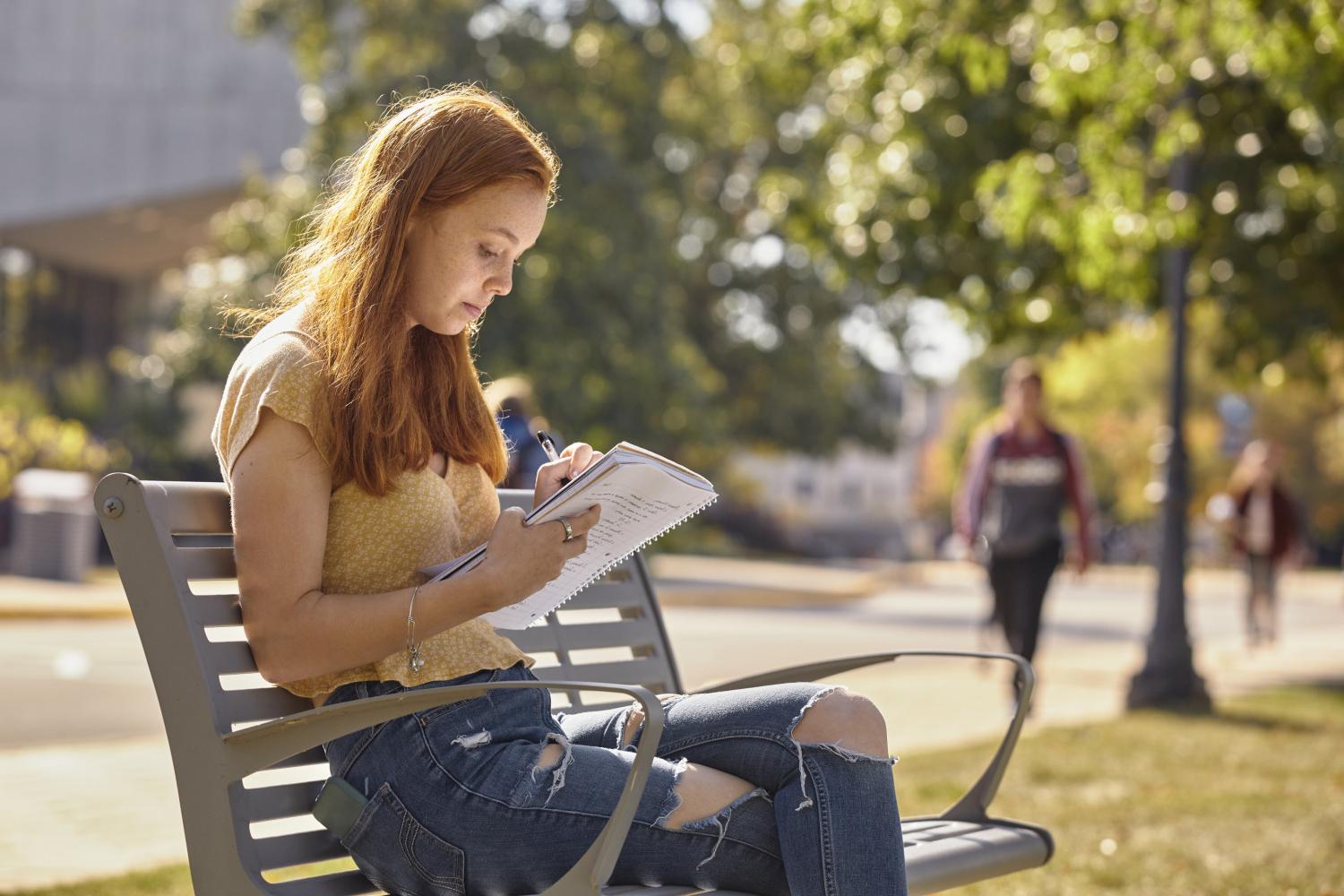 A <a href='http://3z26.umkt.net'>BETVLCTOR伟德登录</a> student reads on a bench along Campus Drive.